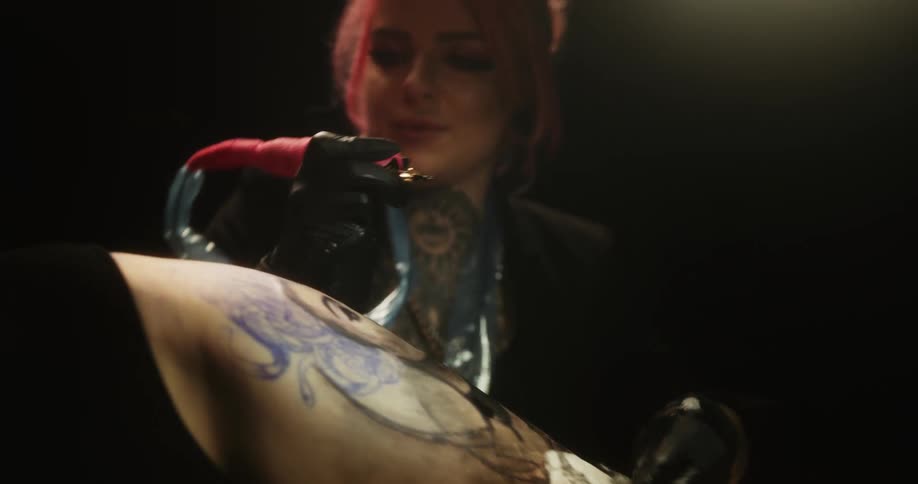 Female tattooist with pink hair tattoos and wipes clients skin as she works