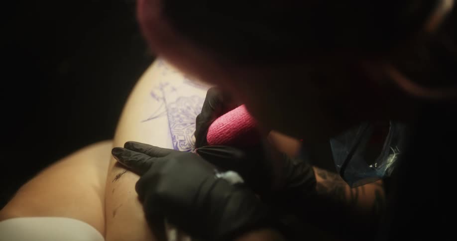 Tattoo artist injects ink and pigments just underneath the skin with a small sanitized needle at tattoo studio