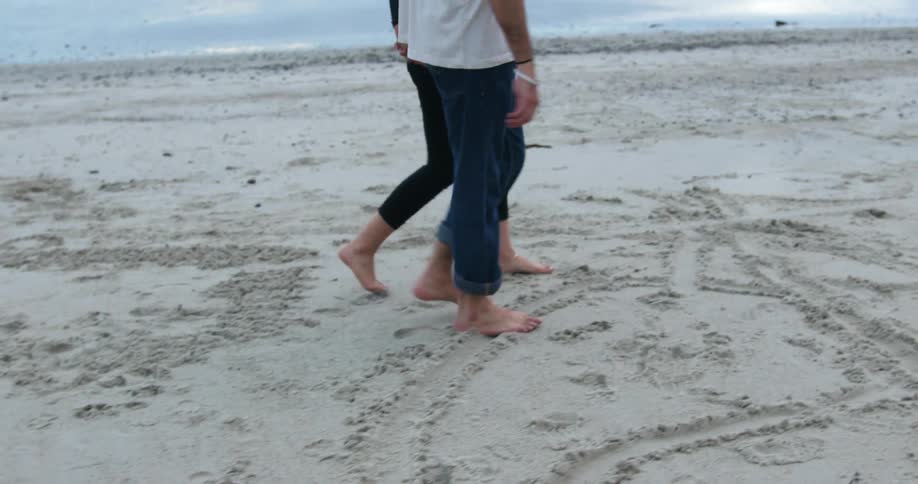 A man and woman walk hand in hand on a beach