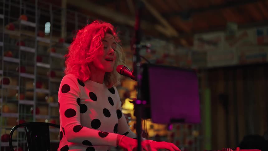 Female singer playing a keyboard performs on stage on a small venue