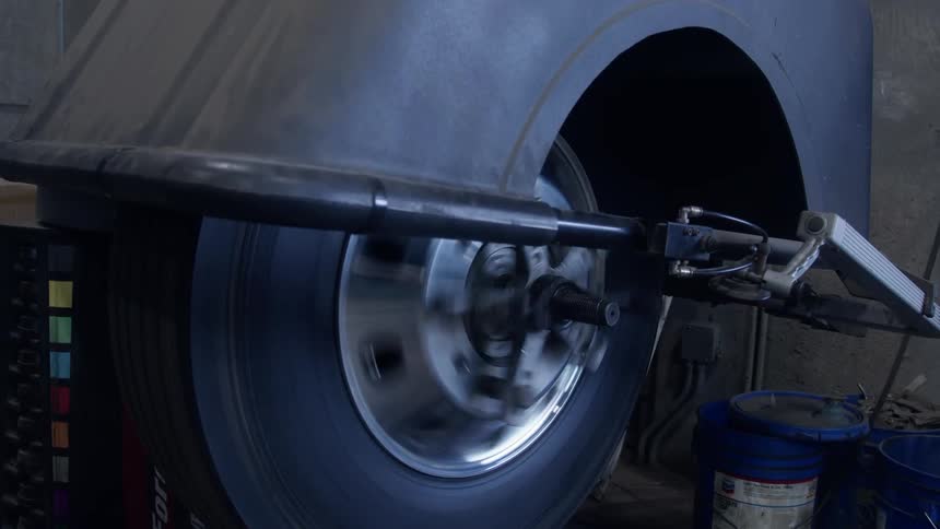 Technician lowers the hood of a tire balancer machine spinning a wheel
