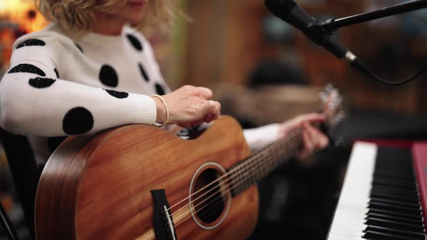 A woman in a bar adjusts her guitar before playing as a man runs behind her