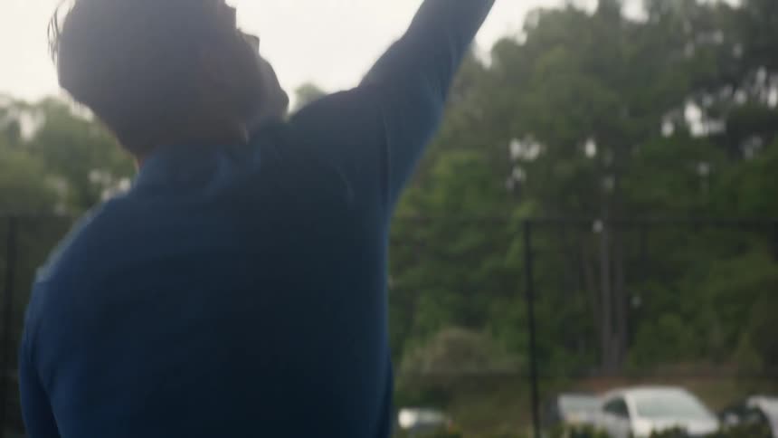 A teenage boy on a tennis court bounces a tennis ball and then serves it