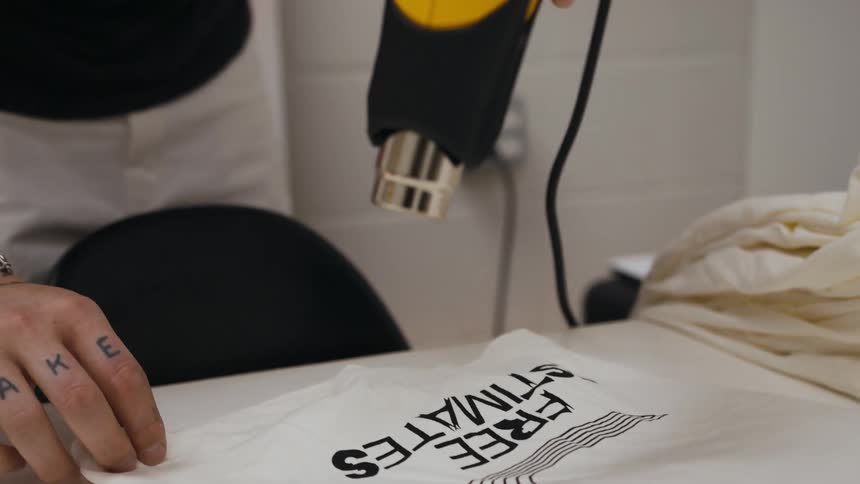 Person with multiple tattoos applies heat gun to printing on fabric