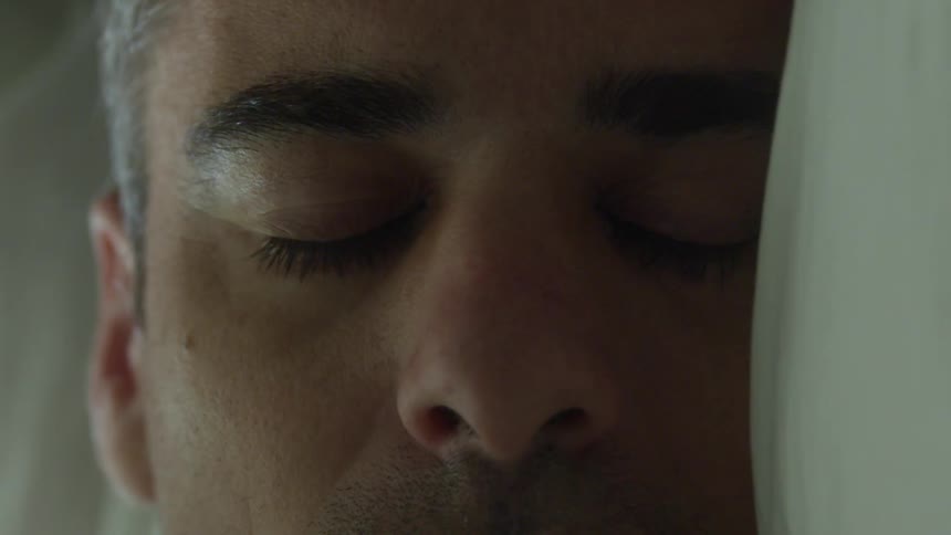 A man is sleeping and then he opens his eyes and rubs his face with his hand