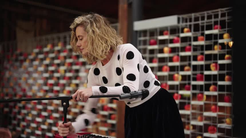 A woman is standing in front of a display of apples as she sets up a microphone on a stand