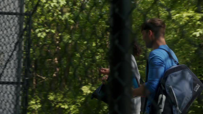 A teenage boy and girl talk and laugh as they walk on to a tennis court