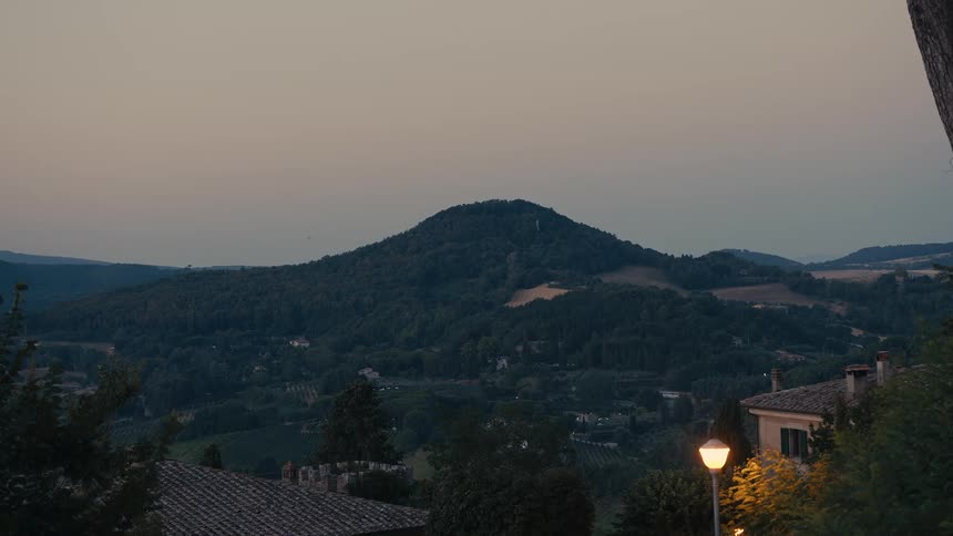Buildings sit on hill overlooking town and forest across from forest covered mountain