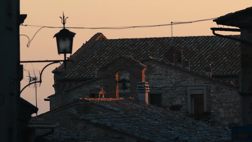 Birds sit on the roof of an old building with a bell in front