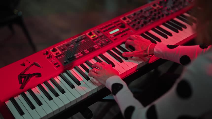 A stage light shines on a woman wearing a polka dot shirt as she plays the keyboard