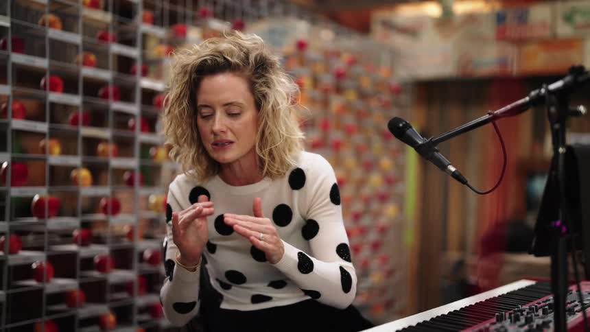 Musician sitting at keyboard near microphone gestures while trying to explain