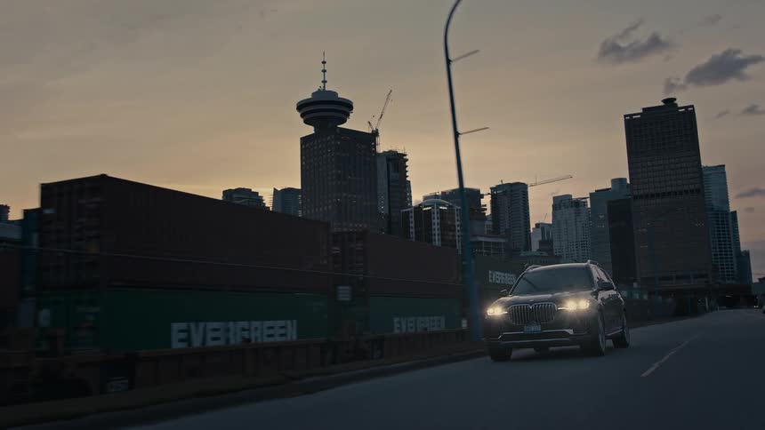 Car drives along highway paralleling train with city skyline in the background