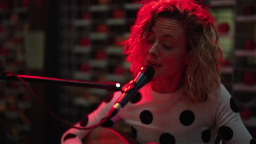 A woman is playing the guitar in a studio and is singing