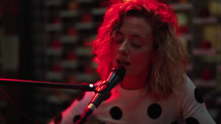 A woman is behind a keyboard as she plays an acoustic guitar and sings into a microphone