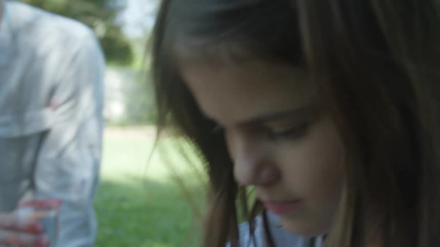Parents smile while they sit on ground in backyard watching daughter paint