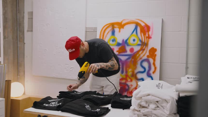 Man uses heat gun to dry graphics printed onto t shirts while standing in workshop