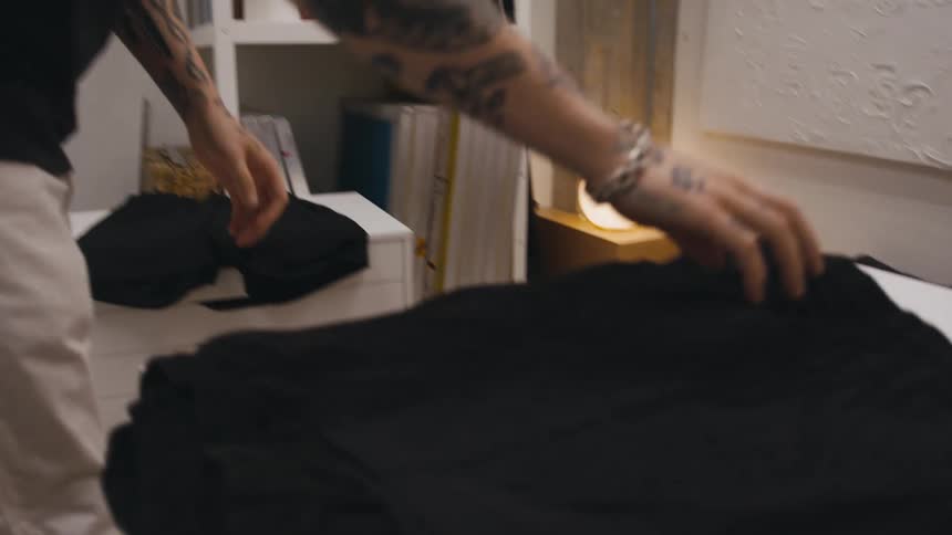 A man is standing in a room picking out clothers and setting them aside