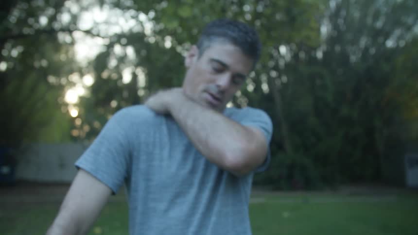 Man massages his arms and legs on the backyard at evening