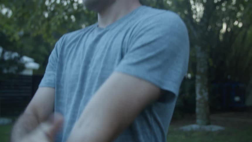 A man is standing outside in his yard patting his arms and shoulders with his hands