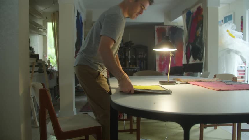 Artist sits down to page through sketchbook in artist studio