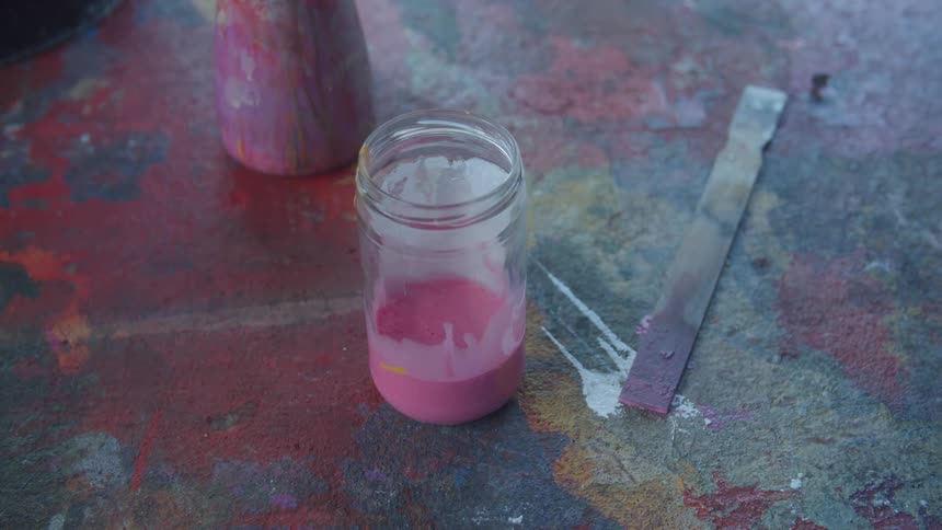 Someone pours pink paint into a jar and then pours in darker paint to mix