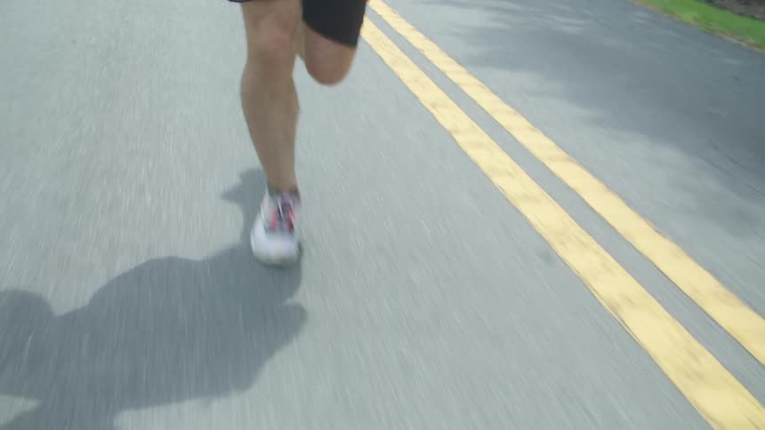 A man wearing shorts is jogging on a street near the yellow lines