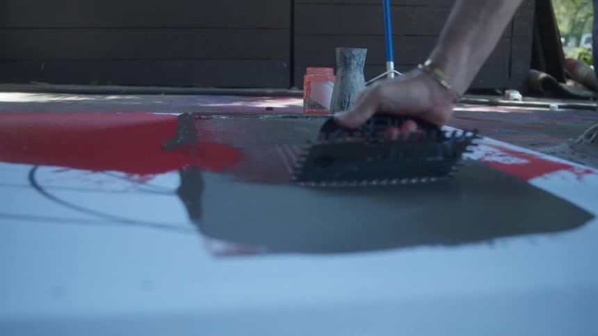 Close up of a painter using a scrape to texture paint over canvas