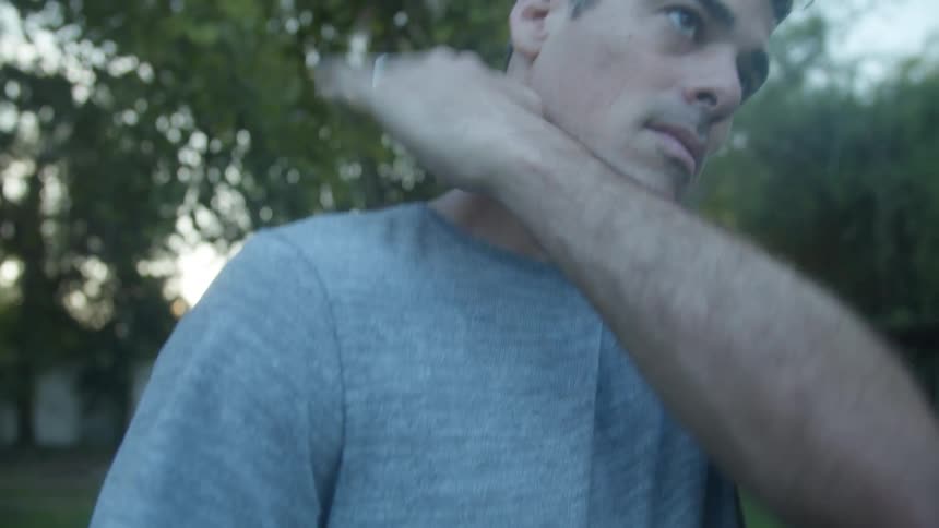 A man stands in his yard and pats up and down his arm and on to his shoulder