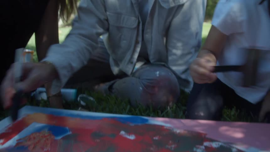 Family sits on lawn in backyard painting on canvas together