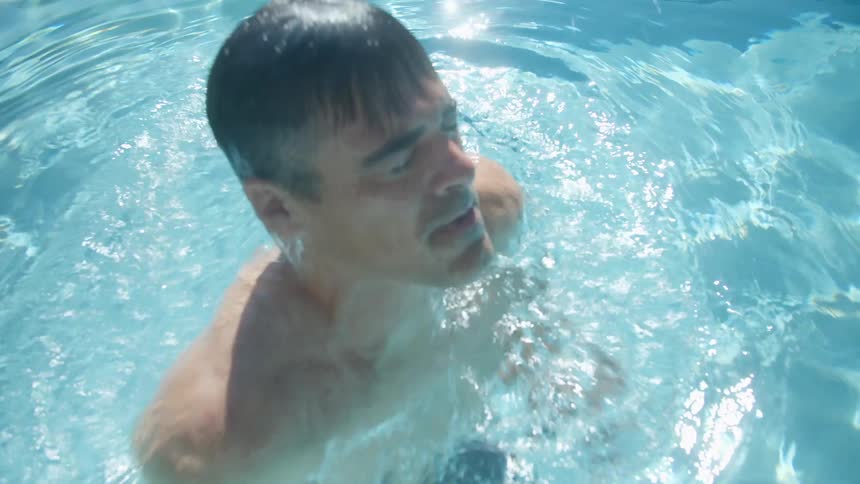 A young white man is swimming outside of a pool in the day time