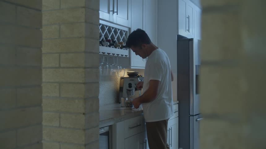 A man opens a kitchen cupboard and takes out a cup and sets it on the counter and pours himself a cup of coffee and puts milk in it before he walks out