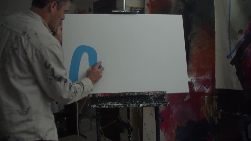 Painter standing in artist studio applies paint to canvas