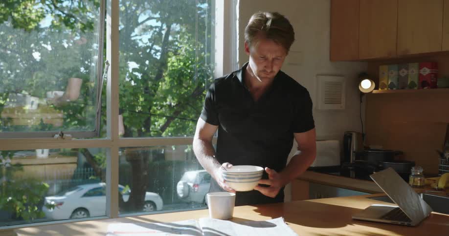 A man pours himself a cup of coffee and reads the paper while eating