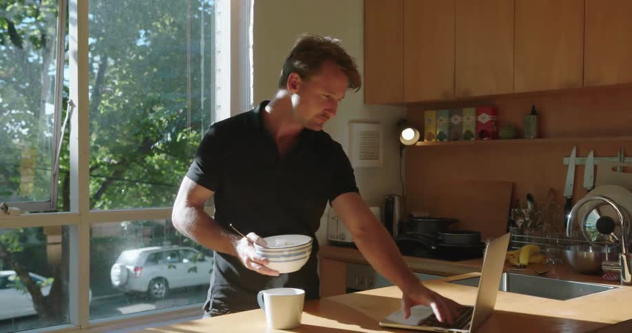 Man holding a bowl typing on a laptop in the kitchen