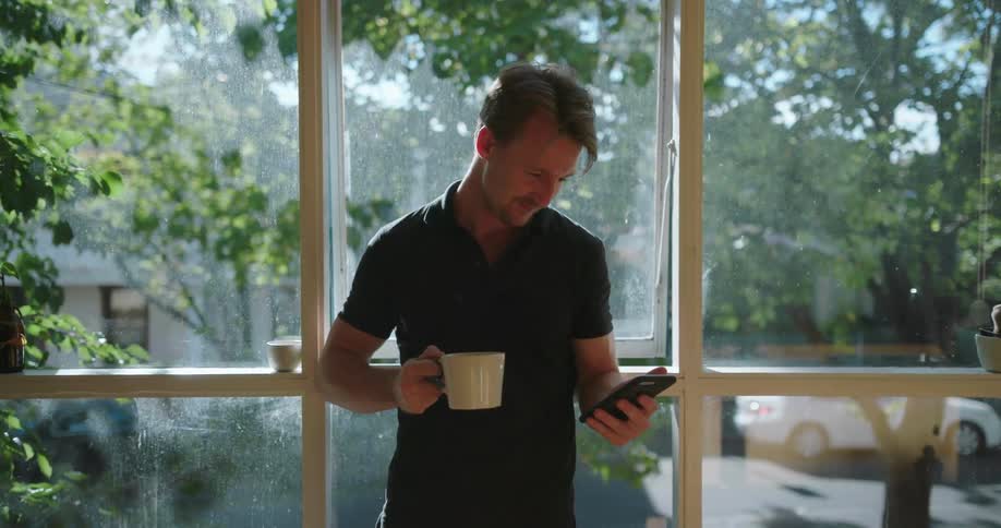 Man drinking out of a mug and looking at his phone