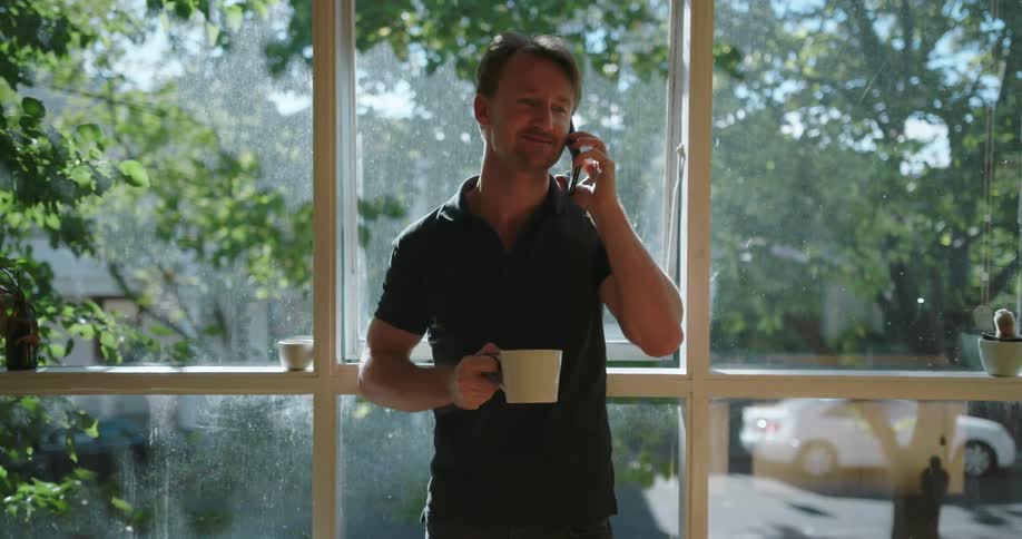 A man talks on the phone holding a steaming cup of coffee