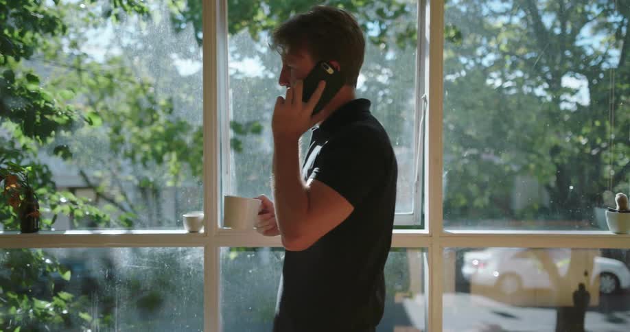 A man talks on the phone holding a steaming cup of coffee