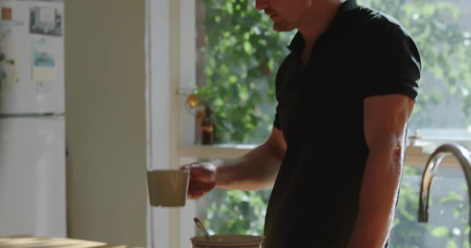 A man types on a laptop one handed and then sips from a coffee mug