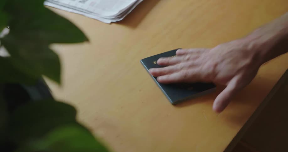 A man picks up a passport and keys from a table