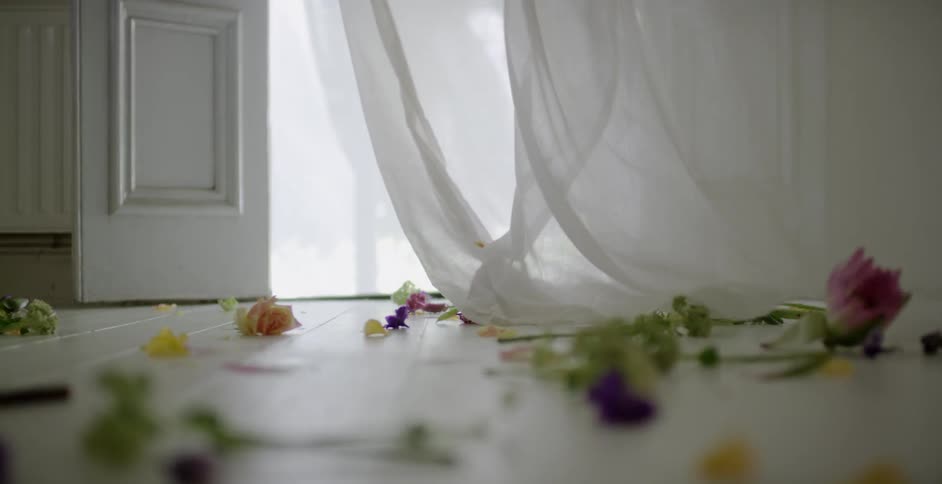A curtain blows near a floor covered with flowers