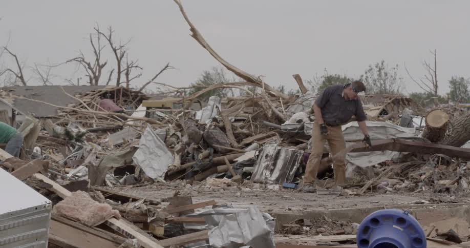A man walks among debris lifting a large item