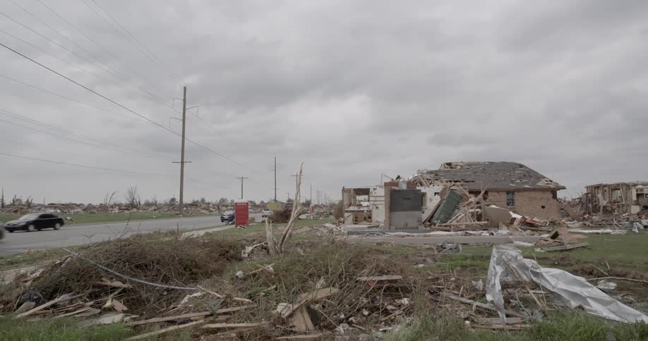 Cars drive past damaged homes