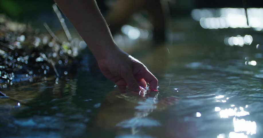 A person dips a water sample kit in to a river and fills it