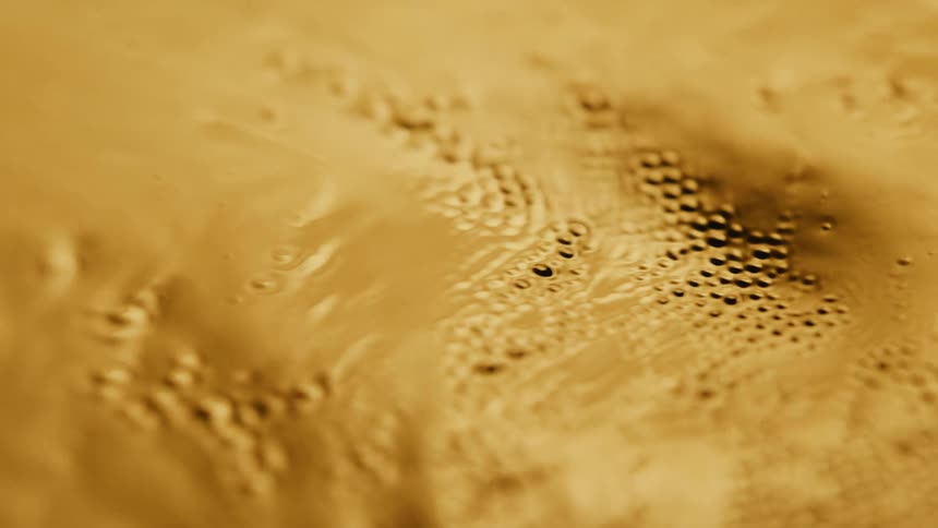 Light shines on a gold substance with many small holes as it ripples and moves