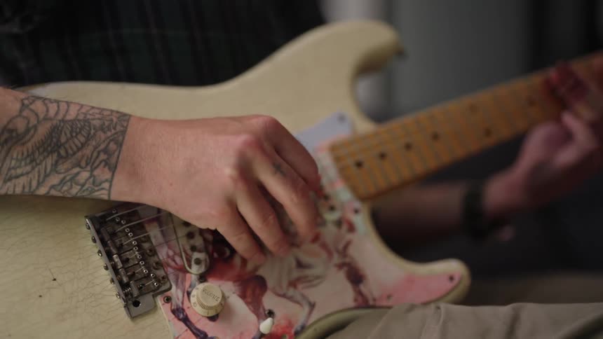 A man is sitting down playing an electric guitar