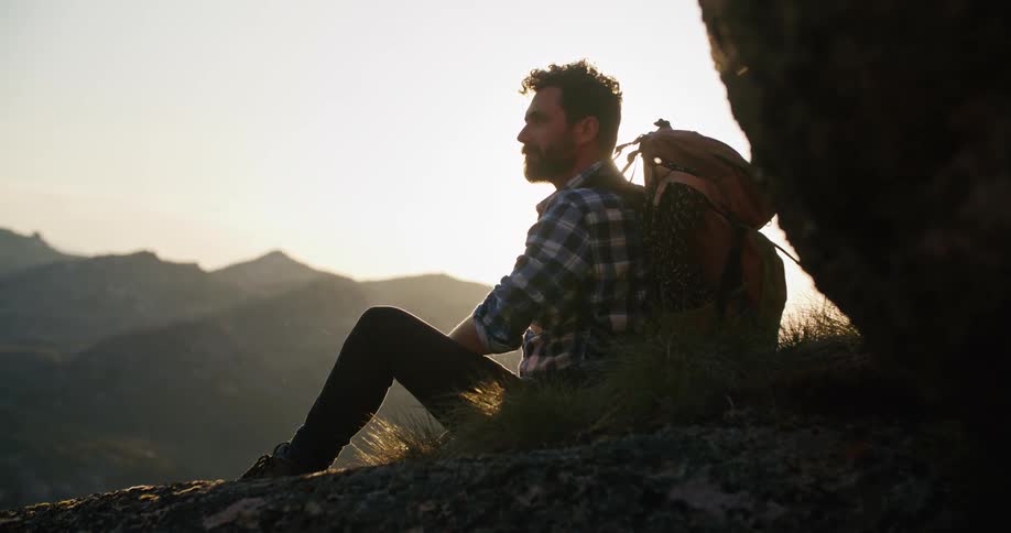 A man out hiking sits on a mountain top and looks at the view