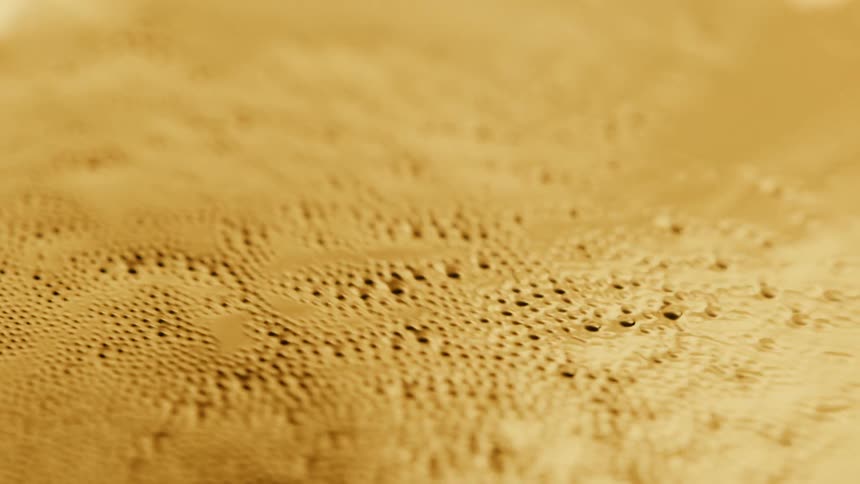 Surface of a shiny golden thick liquid disturbed by a small bubbling wave