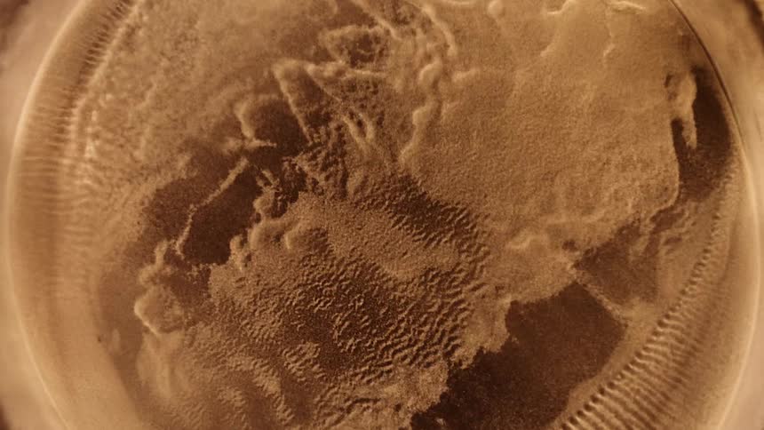 A gold substance vibrates and pulsates as it becomes a powder and spreads as it bounces