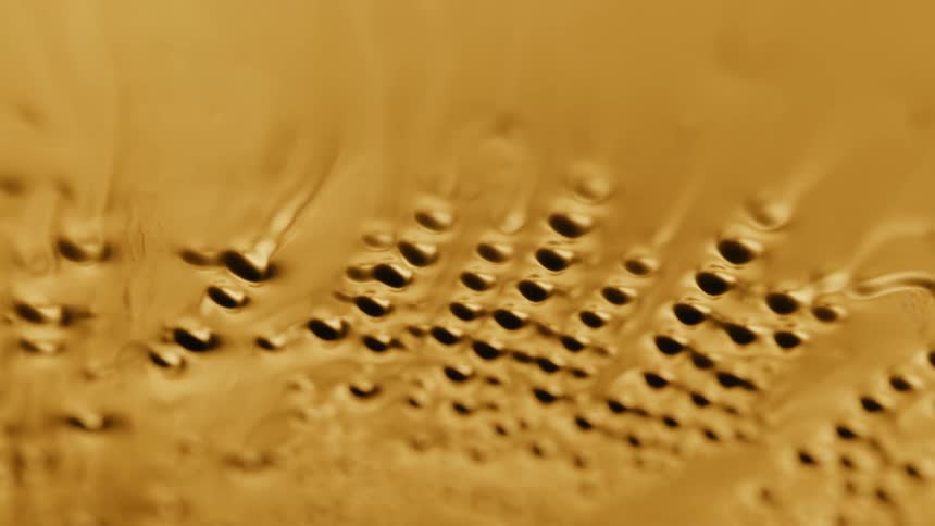 Light shines on a gold organic liquid substance and holes emerge as it ripples and moves and then melts down