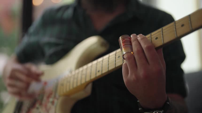 A man plays a guitar using a slide on finger